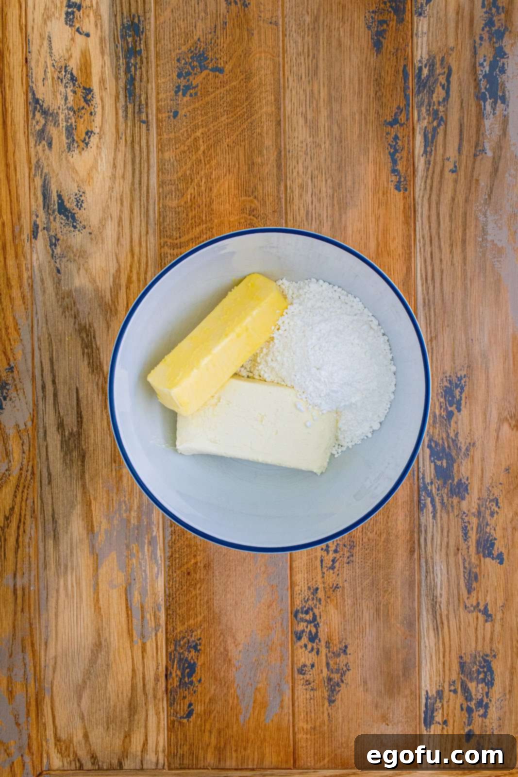 A bowl filled with softened cream cheese, butter, and a mound of powdered sugar, ready to be mixed into creamy frosting.
