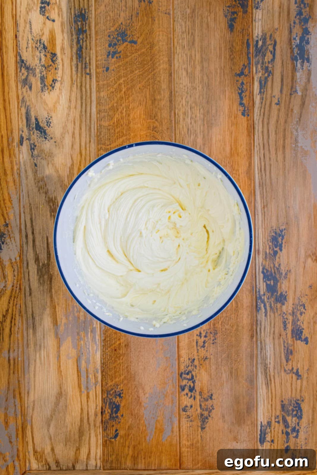 A rich, smooth, and creamy buttercream frosting fills a white mixing bowl, ready for spreading.