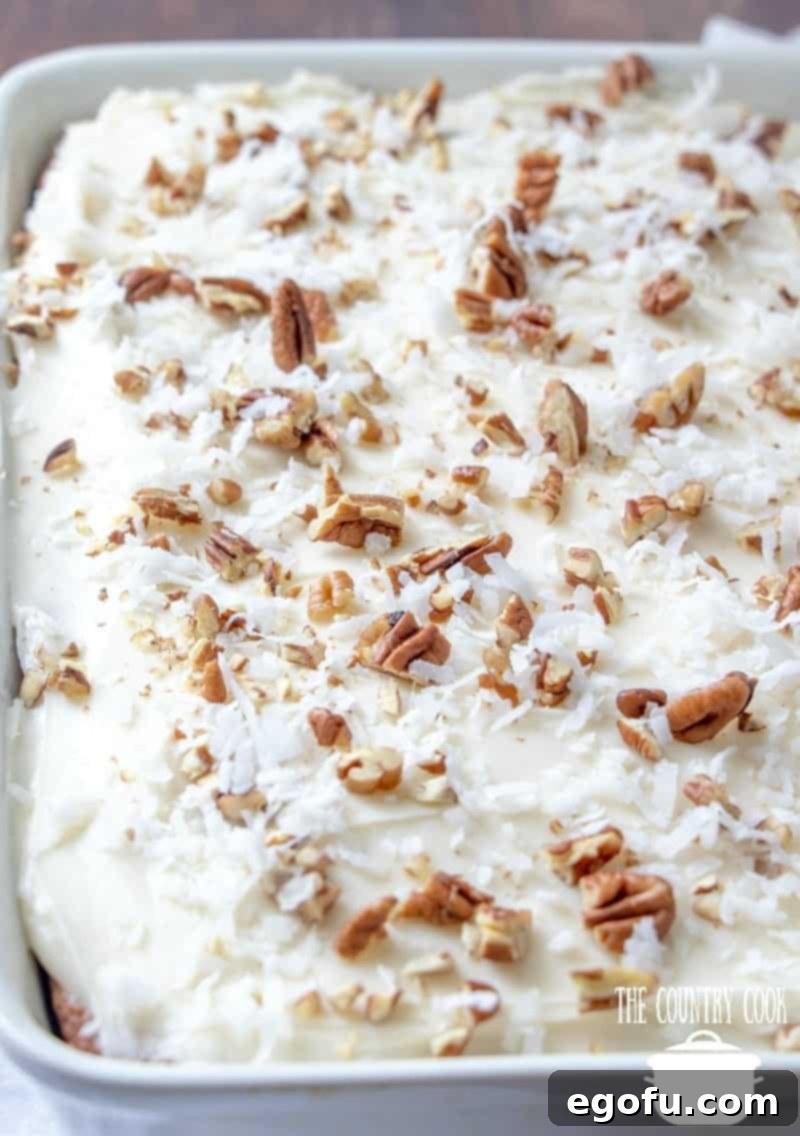 A beautifully frosted homemade Italian Cream Cake in a white baking dish, generously topped with chopped pecans and shredded coconut.