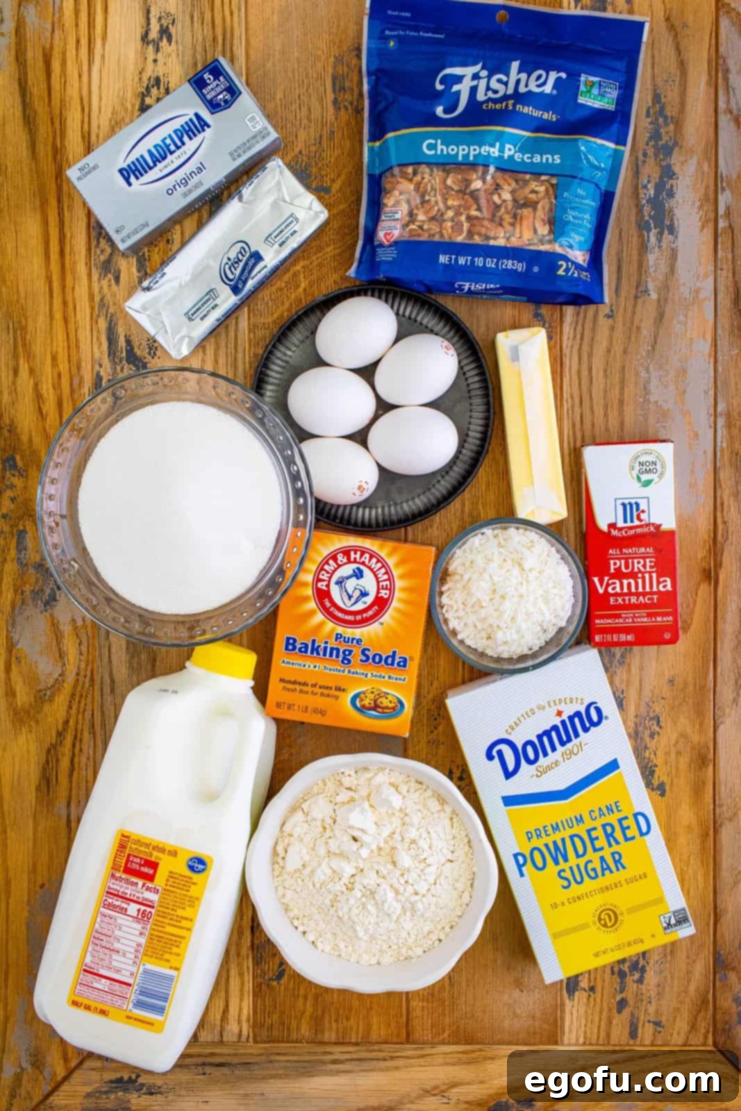 A vibrant flat lay of key ingredients for Italian Cream Cake: cream cheese, shortening, eggs, buttermilk, pecans, butter, vanilla extract, shredded coconut, all-purpose flour, and powdered sugar.