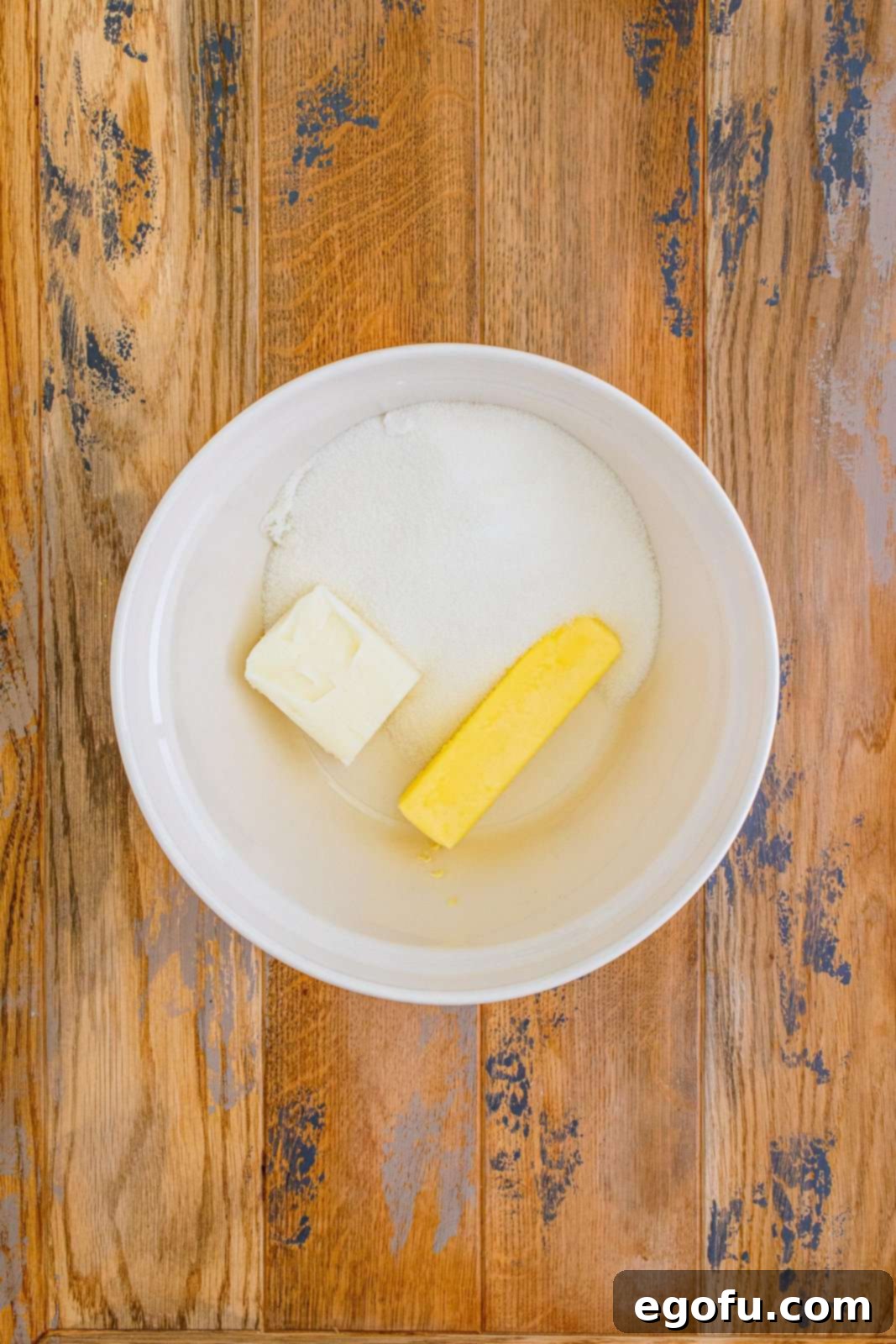 Close-up of butter, shortening, and granulated sugar being creamed together in a white mixing bowl for the Italian Cream Cake base.