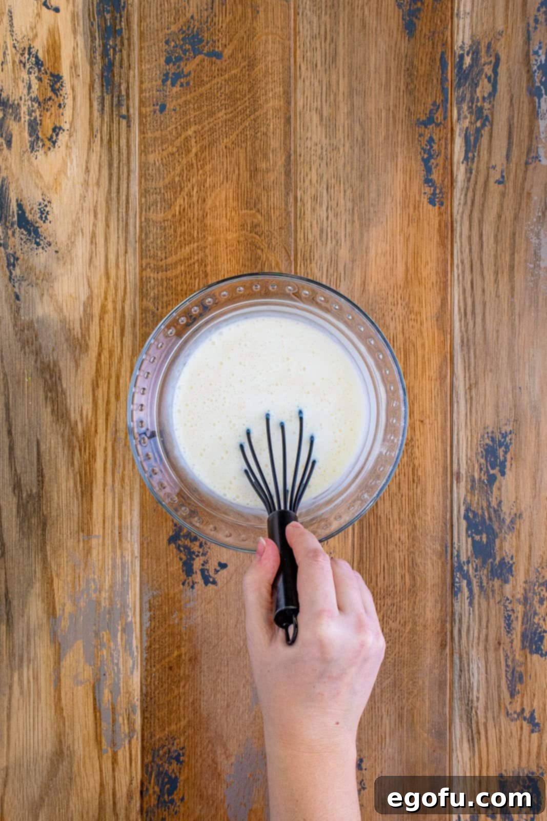 Buttermilk, vanilla extract, and baking soda being whisked together in a clear glass bowl, showcasing the liquid ingredients.