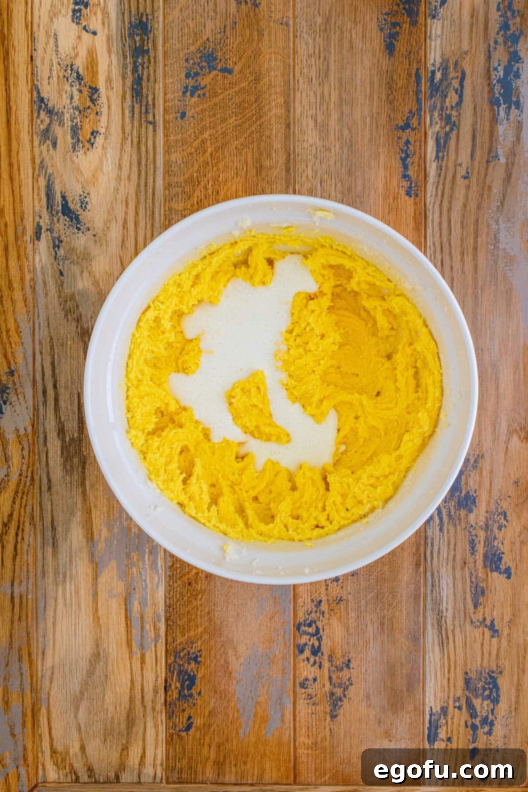 Buttermilk mixture being poured into the large white bowl containing the butter and egg mixture, illustrating the alternating addition step.