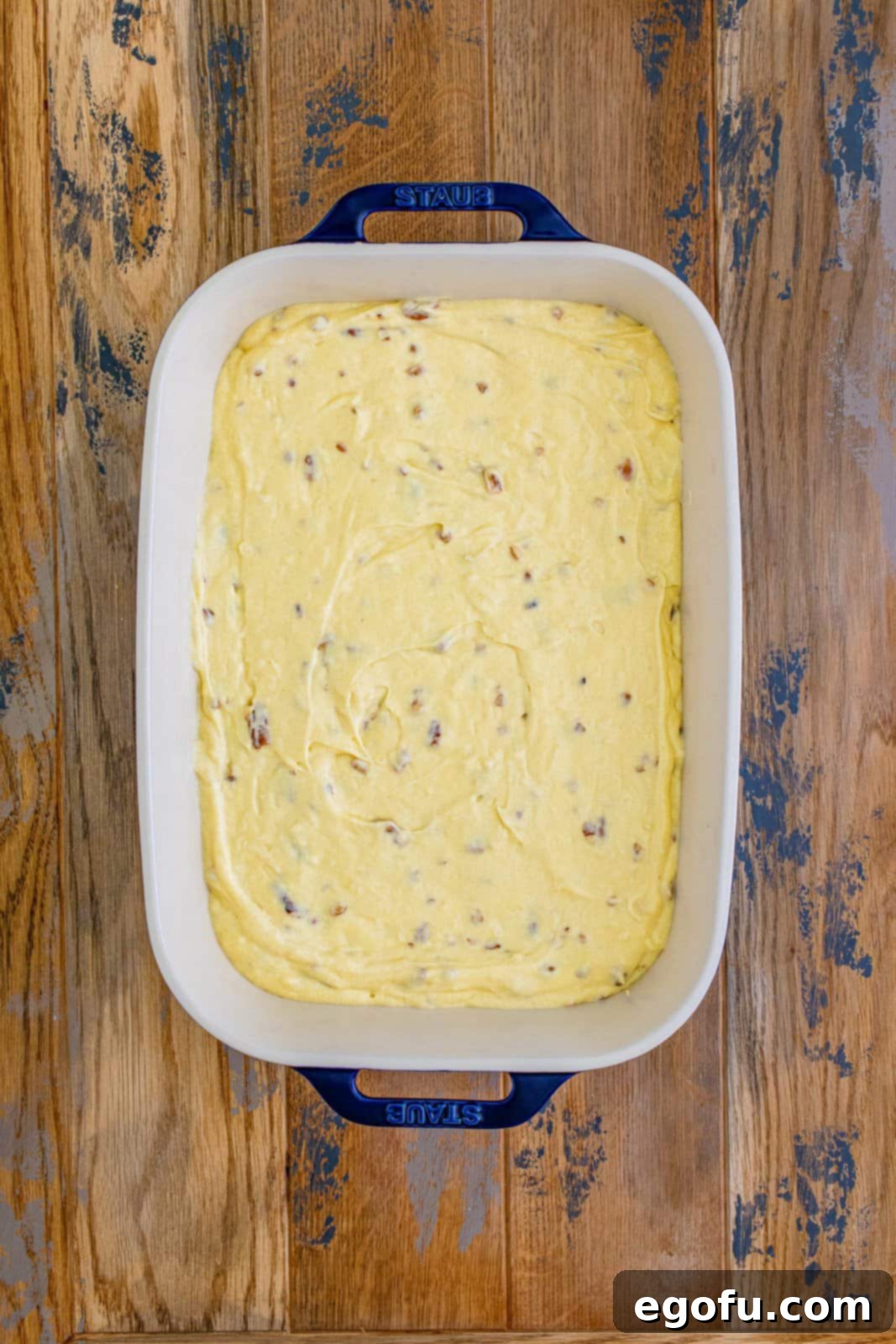 The smoothly spread Italian Cream Cake batter filling a white ceramic baking dish, ready for the oven.