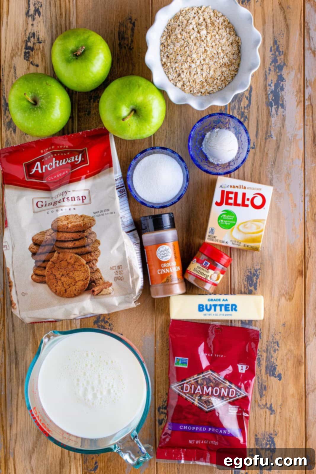 Warm Slow Cooker Apple Crumble 4 A flat lay photograph of all the ingredients: Granny Smith apples, sugar, flour, cinnamon, gingersnaps, quick-cooking oats, pecans, butter, instant vanilla pudding, and nutmeg.