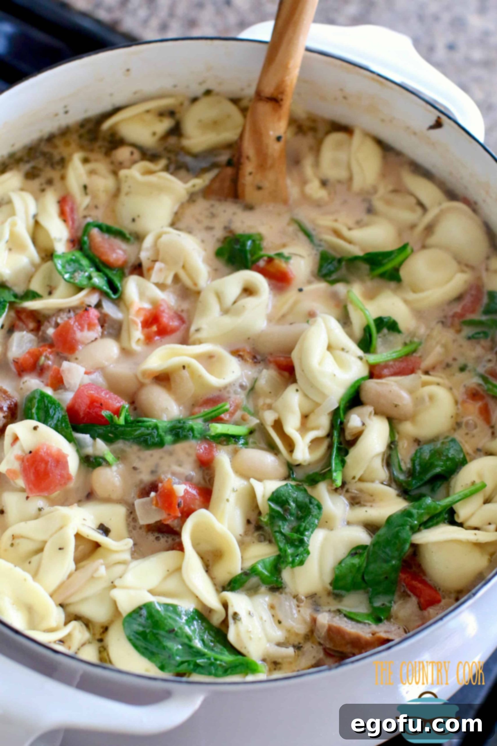 Creamy Tuscan Soup recipe with sausages shown in a white dutch oven.