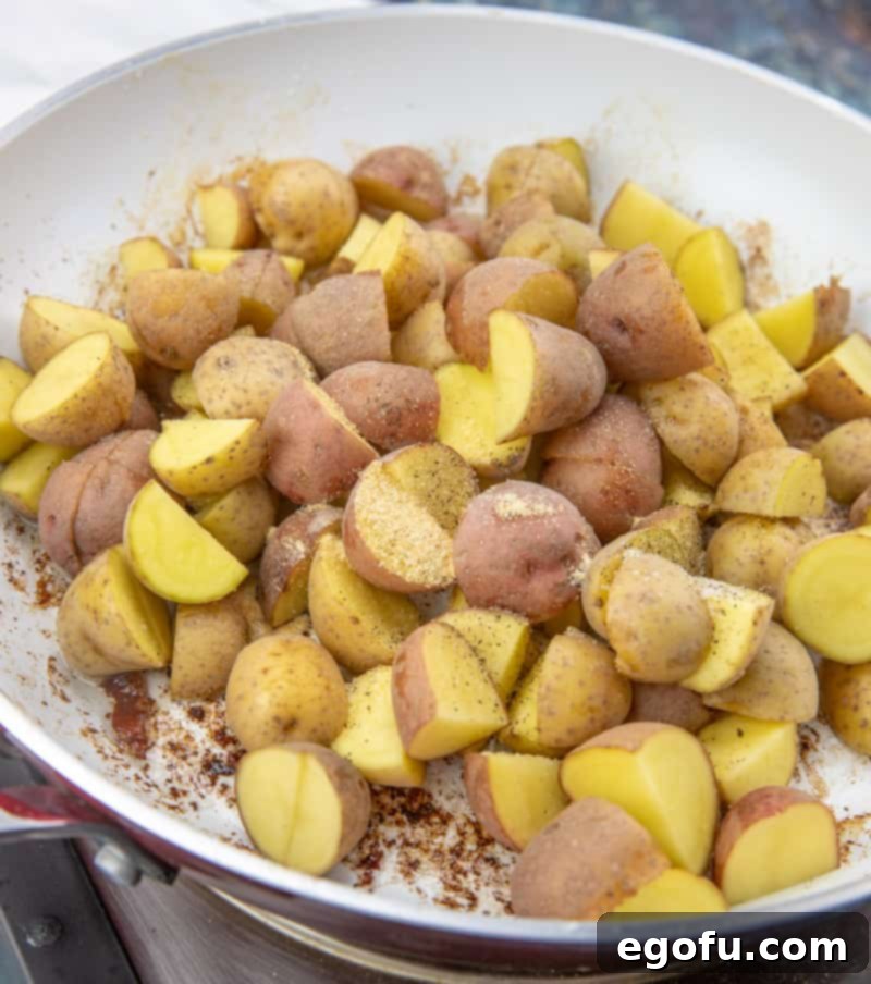 Loaded Cheesy Bacon Chicken and Roasted Potatoes 8 diced baby potatoes in a white skillet with seasonings added.