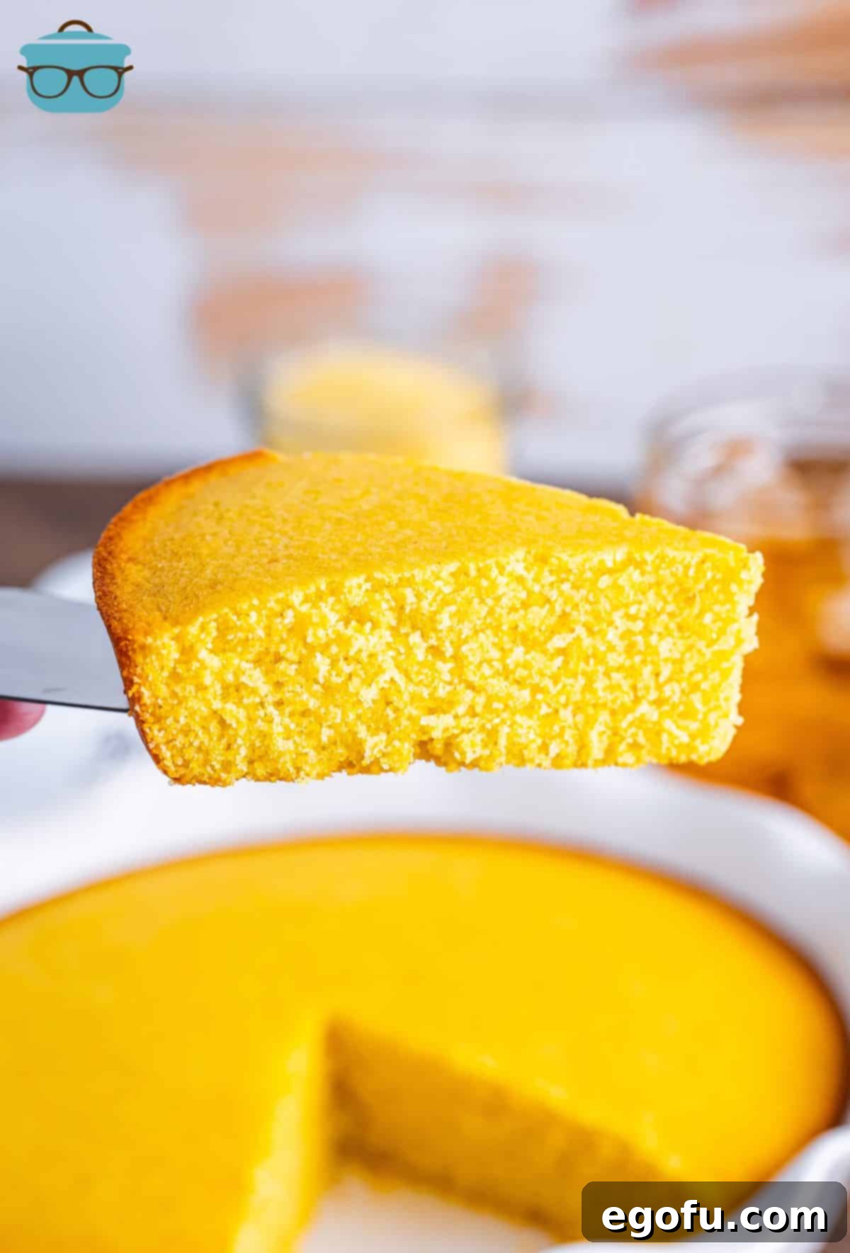 A slice of Sweet Cornbread on a serving utensil held above the rest of the pie plate.