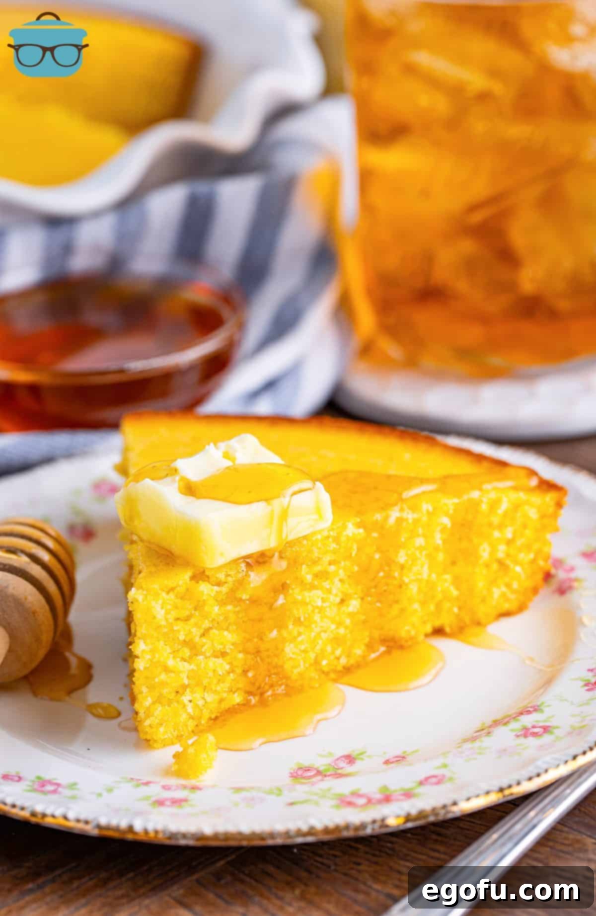 A small plate with a large slice of Sweet Cornbread topped with honey and a pad of butter.