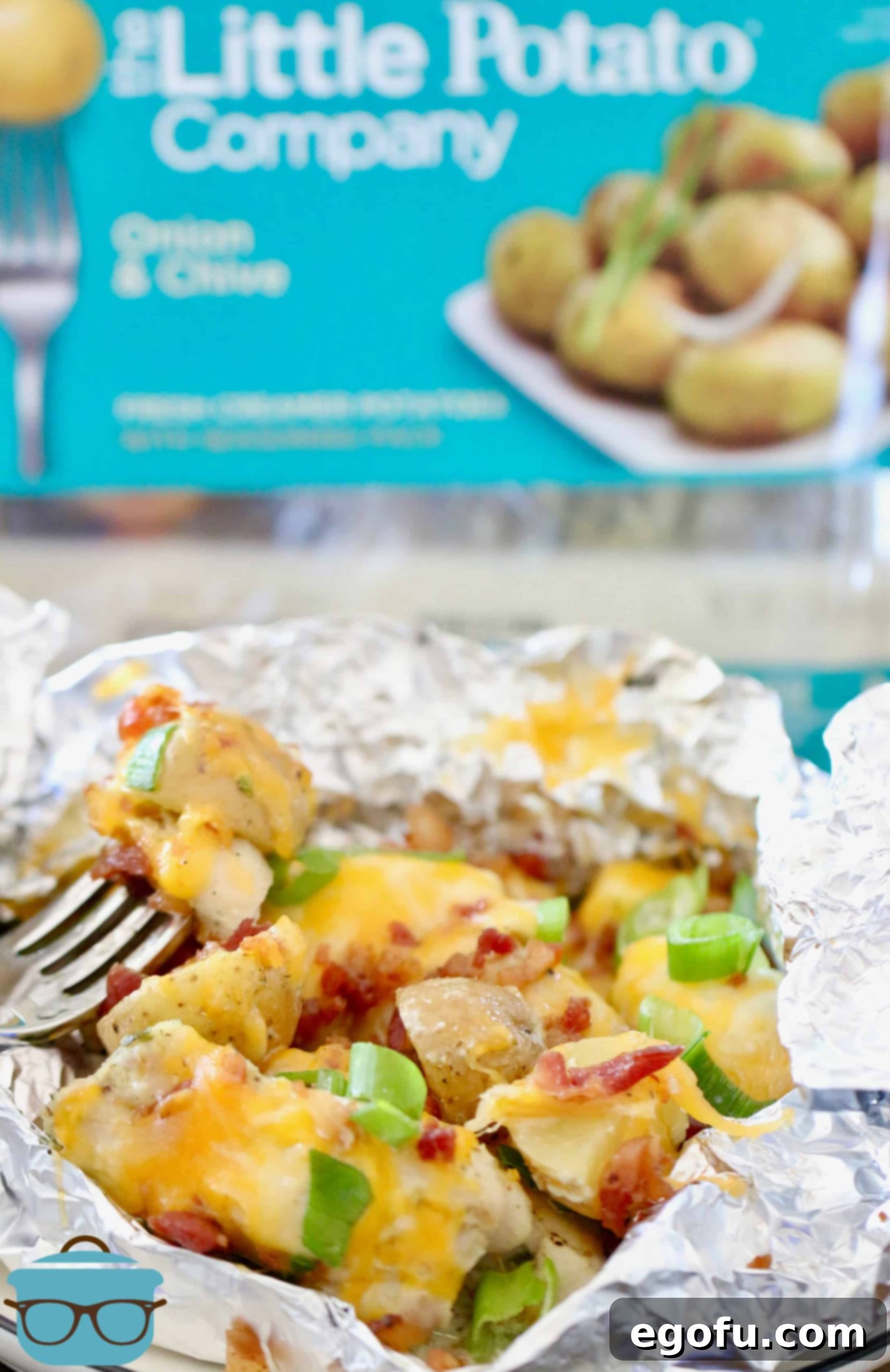 A cooked foil packet opened to reveal diced potatoes and chicken, topped with melted cheese and crispy bacon, showcasing a perfectly grilled meal.