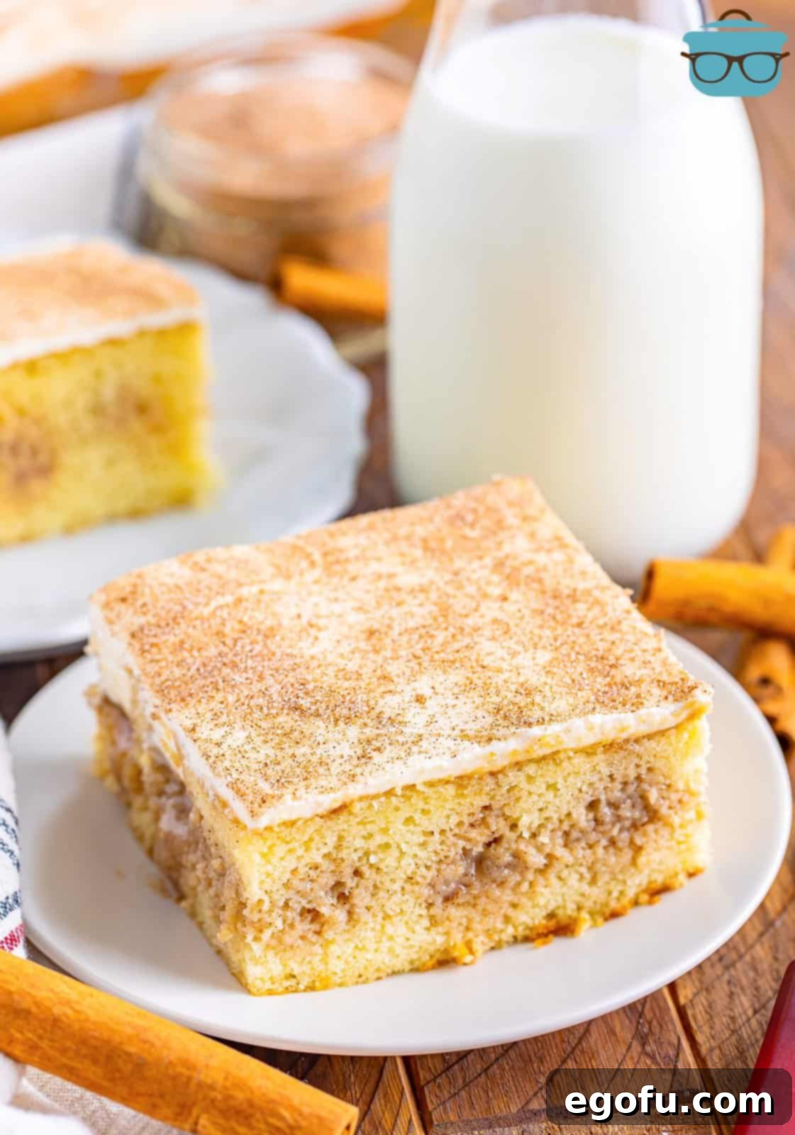 Cinnamon Swirl Poke Cake 8 A tempting slice of Cinnamon Roll Poke Cake on a pristine white plate, with a vintage glass bottle of milk in the soft-focused background, inviting you to take a bite.