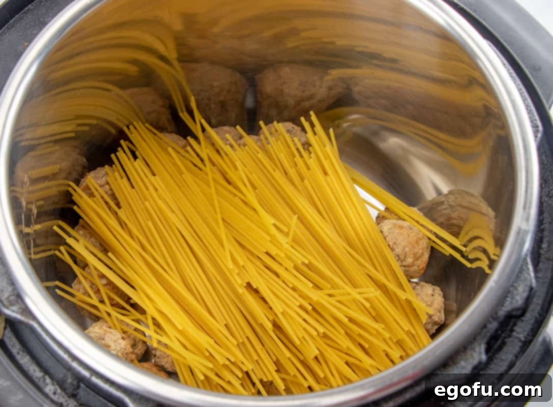 One-Pot Wonder: Instant Pot Spaghetti & Meatballs 6 spaghetti noodles laying on top of meatballs in a pressure cooker.