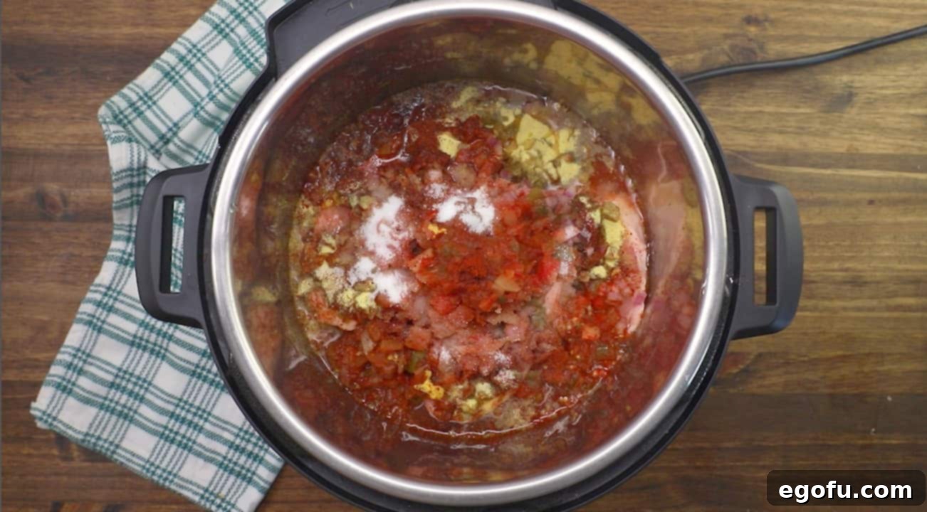 All raw ingredients for Instant Pot Pork Chili, including cut pork, green chiles, red onion, salsa, and spices, are combined at the bottom of a 6-quart pressure cooker, ready for cooking.
