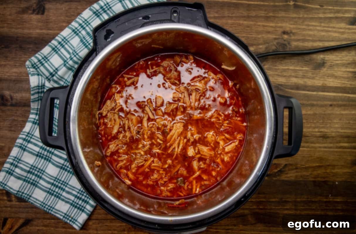 Shredded pork simmering in its rich juices within the Instant Pot, showing the tender consistency after cooking.