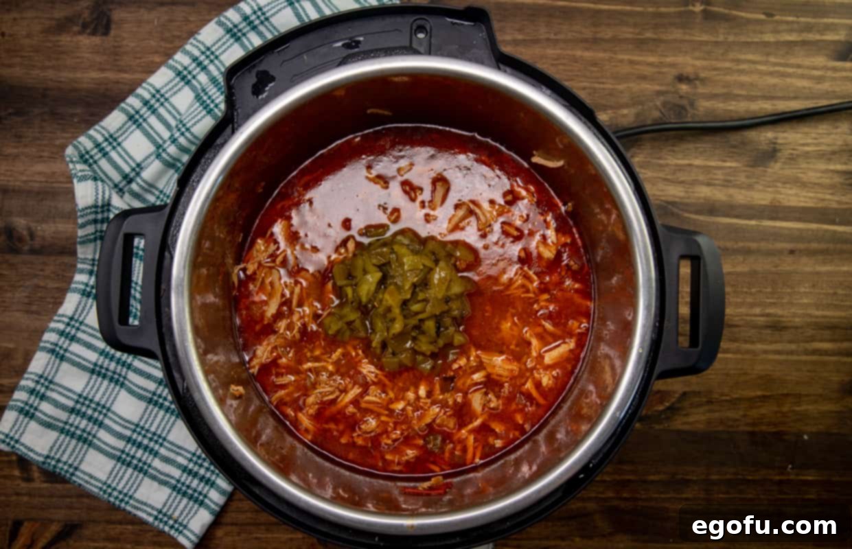 The second can of chopped green chiles being added to the finished, shredded pork chili in the Instant Pot, enriching the flavor.