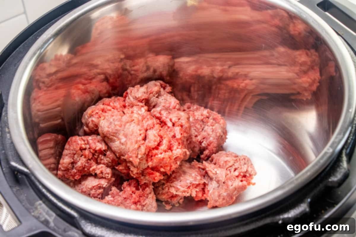 Deconstructed Stuffed Pepper Soup 5 Raw ground beef is placed into the bottom of an electric pressure cooker insert, ready to be browned on the sauté setting.