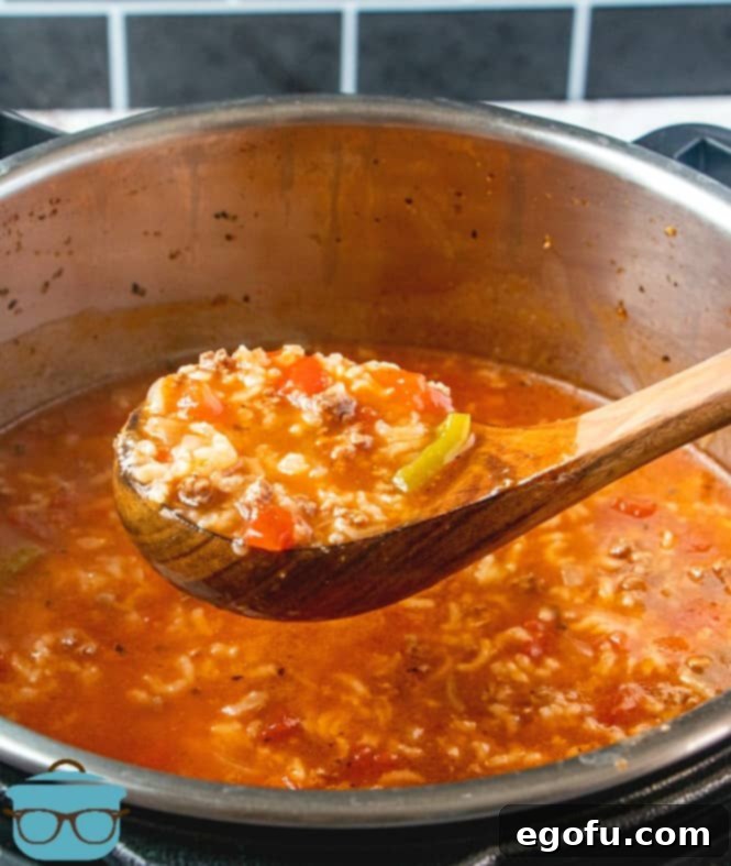 Deconstructed Stuffed Pepper Soup 9 A wooden spoon scoops a hearty portion of fully cooked Instant Pot Stuffed Pepper Soup, rich with ground beef, rice, and vegetables, from the inner pot into a serving bowl.