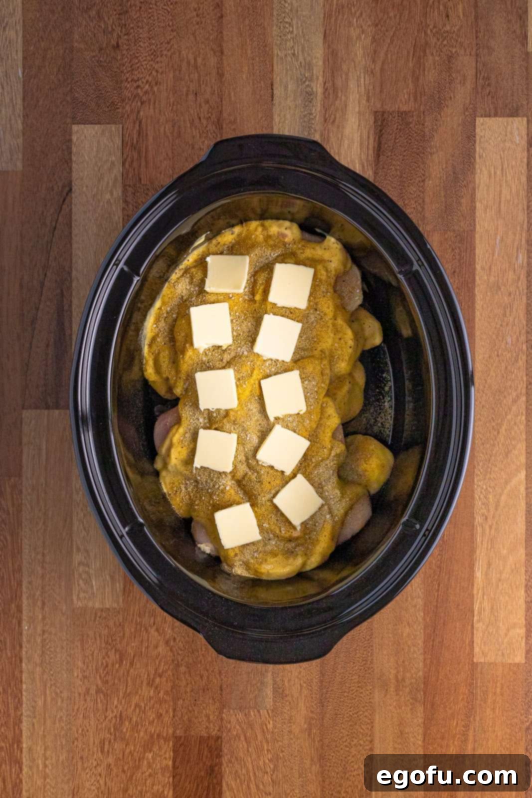 Slices of butter placed on top of cream of chicken soup and seasonings in the slow cooker, ready for the chicken broth.