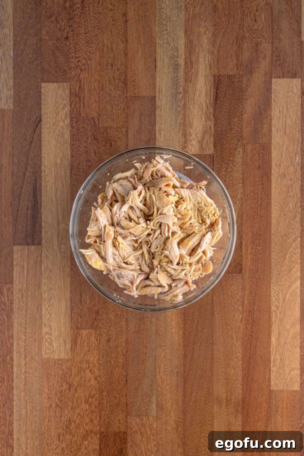 Shredded chicken in a clear bowl, showing its tender texture after slow cooking, ready to be returned to the pot.
