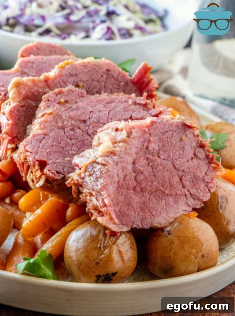 sliced corned beef on a bed of cooked potatoes and carrots with cole slaw in a bowl in the background.