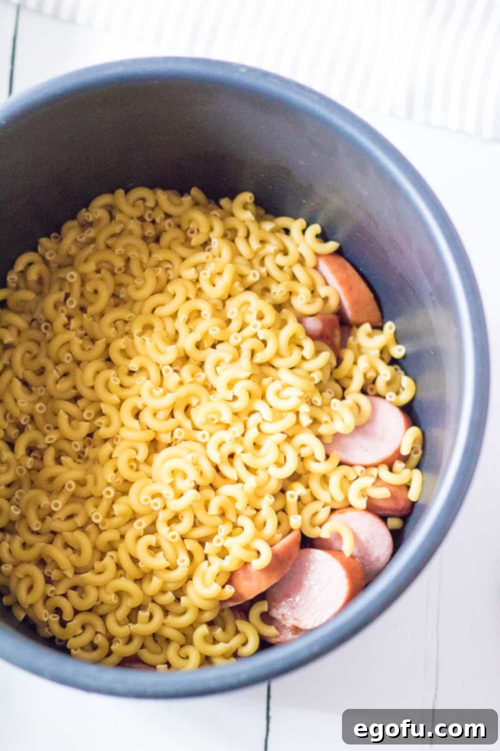 Creamy Instant Pot Sausage Mac and Cheese 6 Elbow macaroni noodles and browned sliced sausage in the bowl of an electric pressure cooker, with water and salt added, ready for pressure cooking.