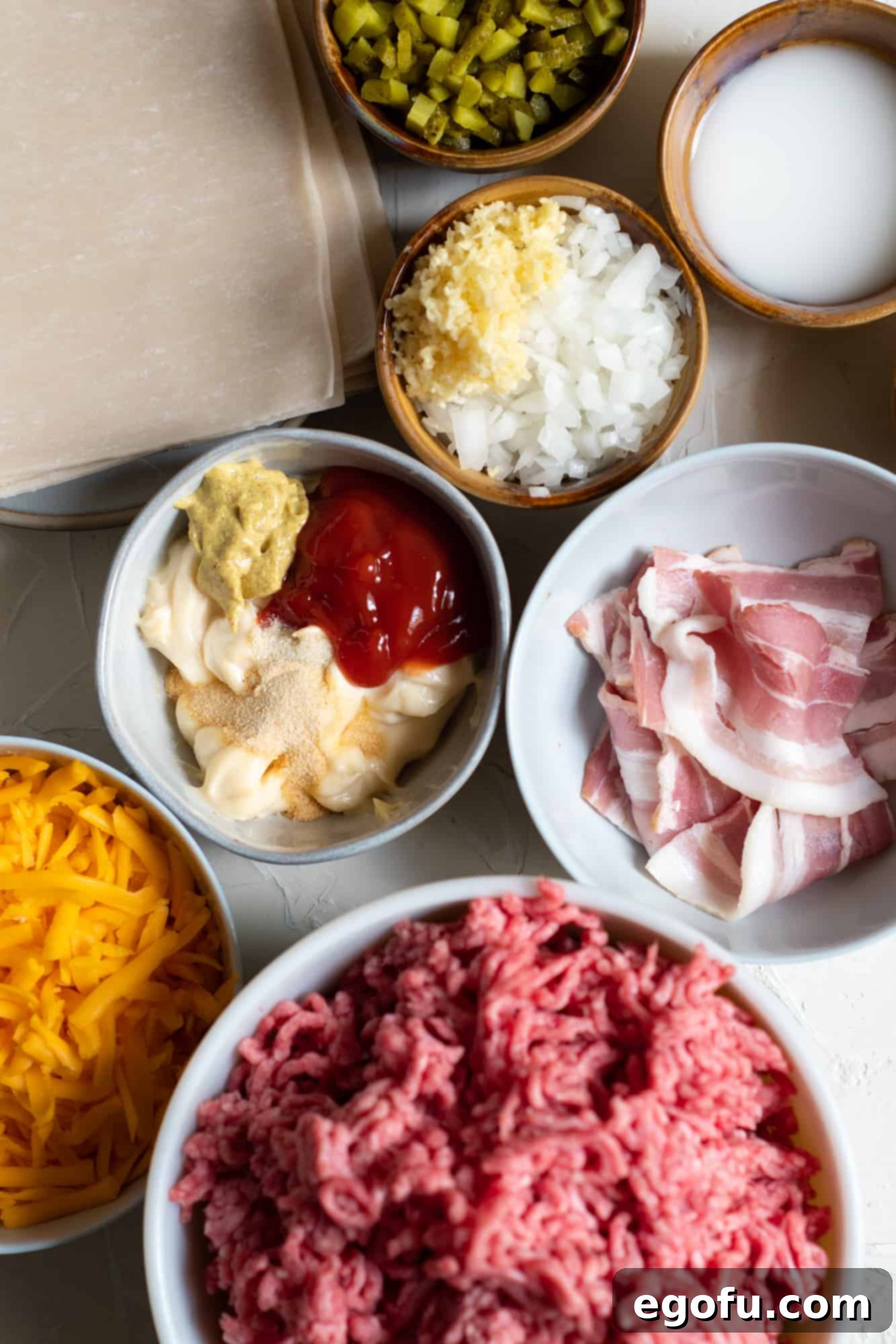 Crispy Cheeseburger Rolls 5 Individual ingredients for Bacon Burger Fried Rolls: bacon, diced onion, minced garlic, ground beef, salt, ground black pepper, shredded cheddar cheese, diced pickles, cornstarch, cold water, egg roll wrappers.