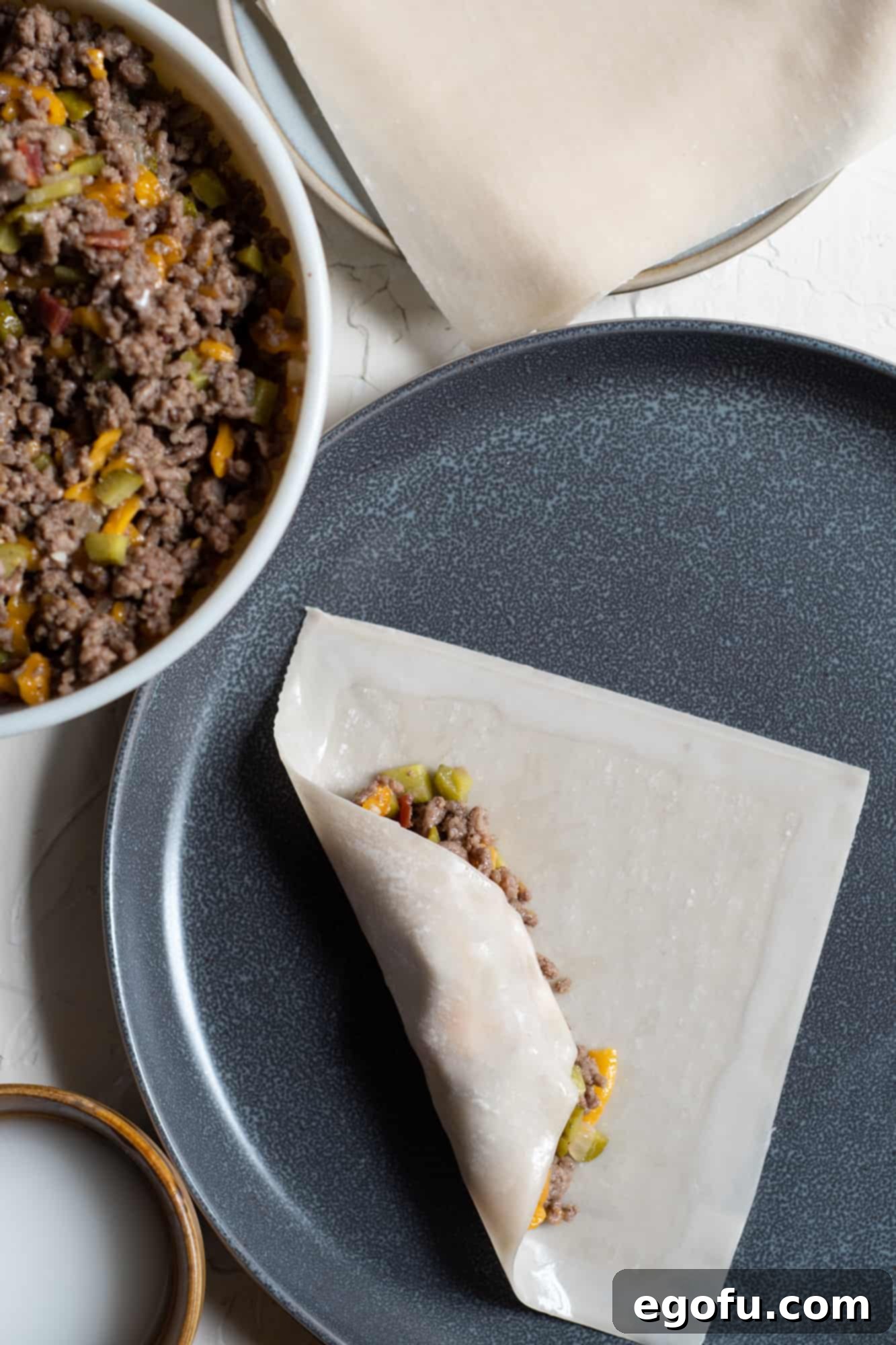 Crispy Cheeseburger Rolls 7 Cheeseburger filling tightly wrapped in an egg roll wrapper, showing the initial roll.