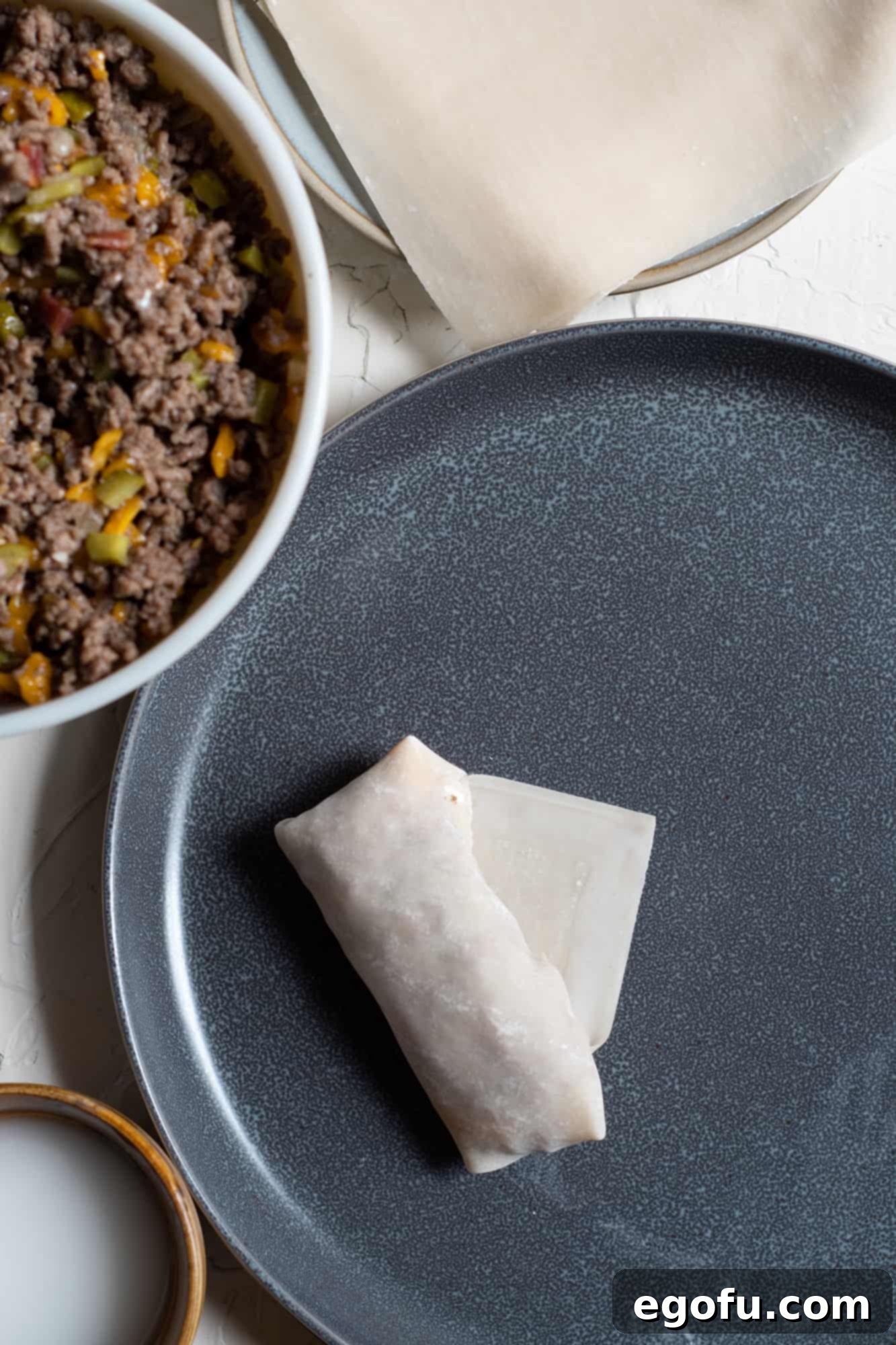 Crispy Cheeseburger Rolls 8 Folding in corners of egg roll wrapper around beef mixture, demonstrating the next step in wrapping.