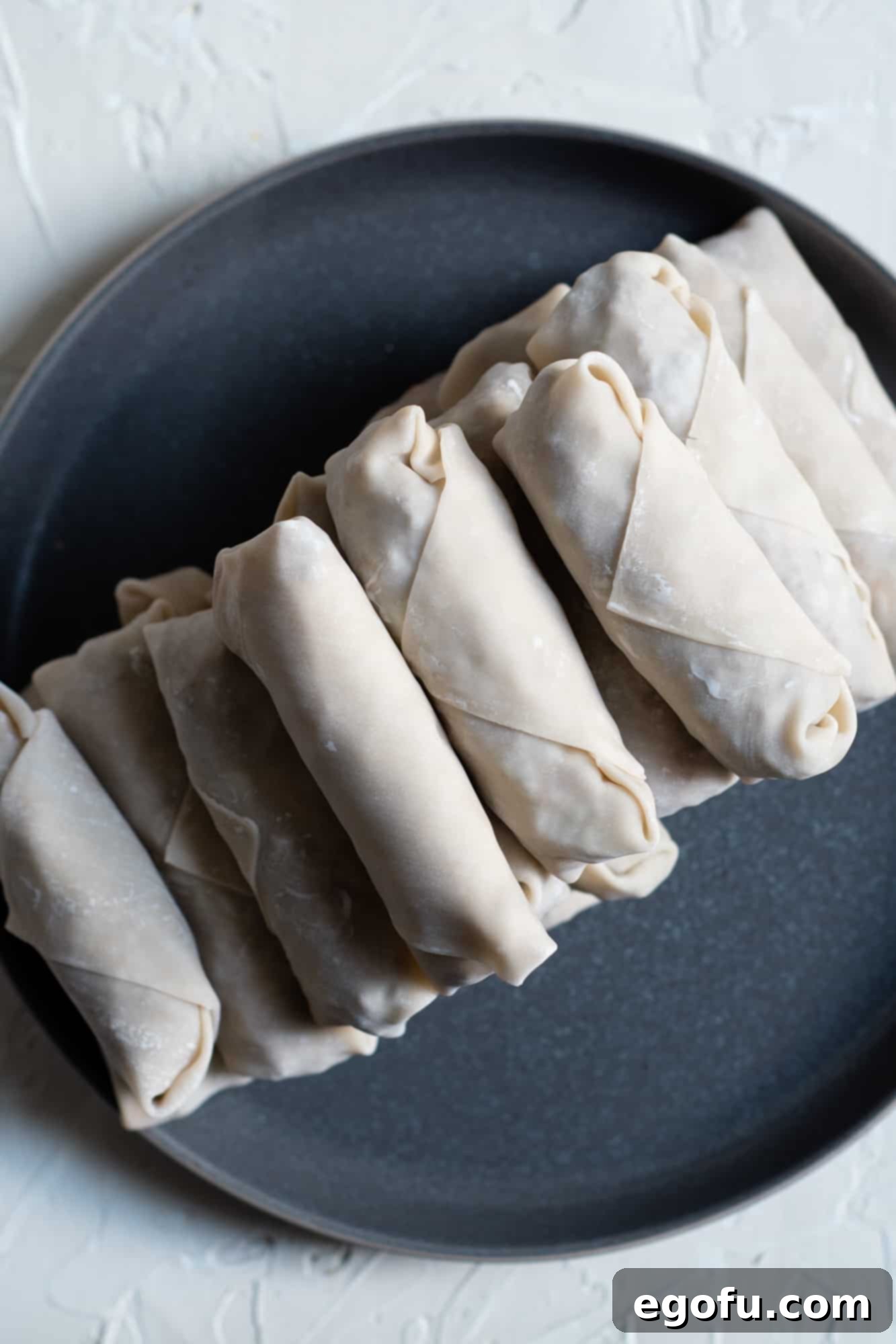 Crispy Cheeseburger Rolls 9 Completed and uncooked egg rolls neatly arranged on a platter, ready for frying.