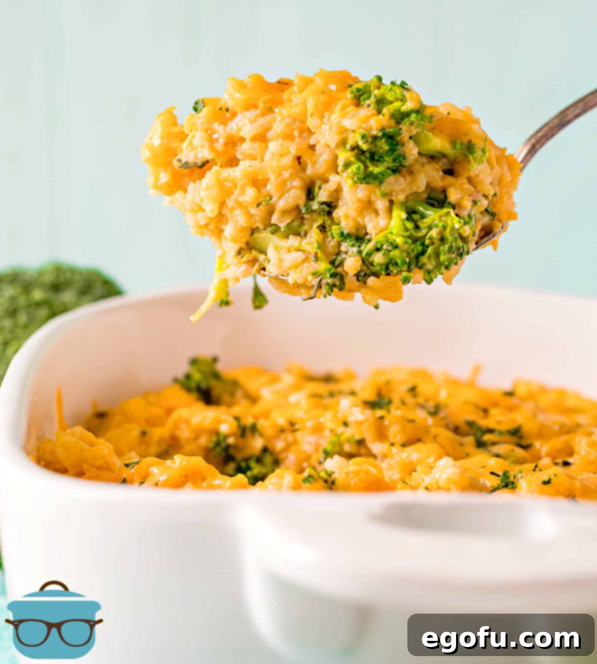 Large spoonful of broccoli rice cheddar casserole being held up over the casserole dish, showing off the perfectly cooked ingredients.