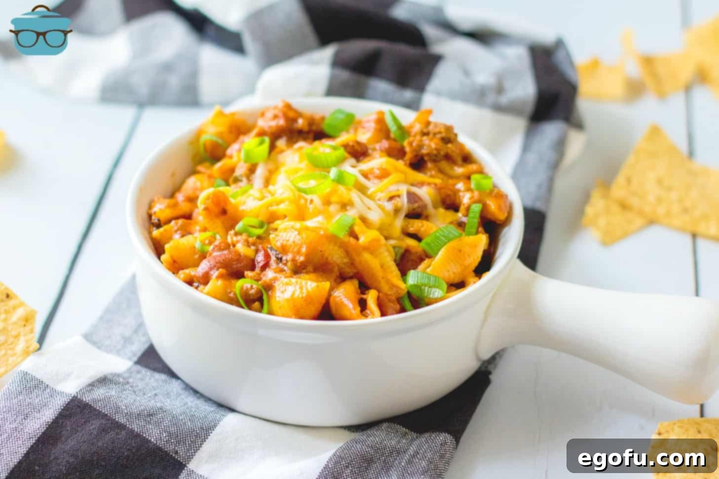 white bowl with handle filled with taco macaroni and cheese, topped with sliced green onions.