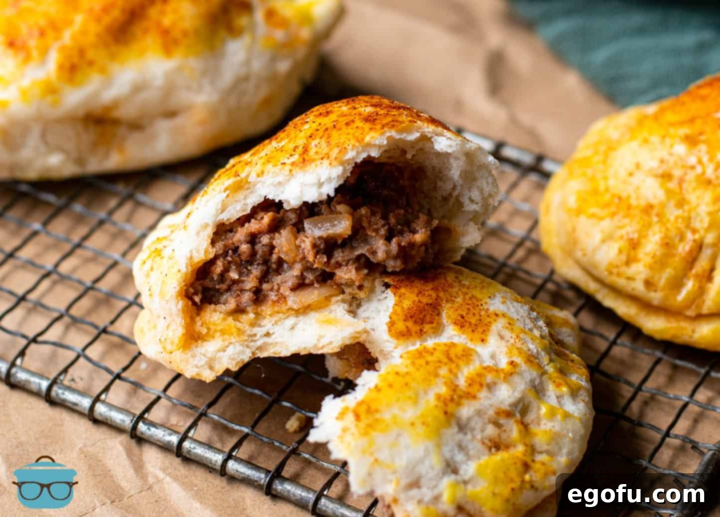 Beef and Potato Biscuit Hand Pies shown on a baking rack, one hand pie is open to show the ground beef inside.