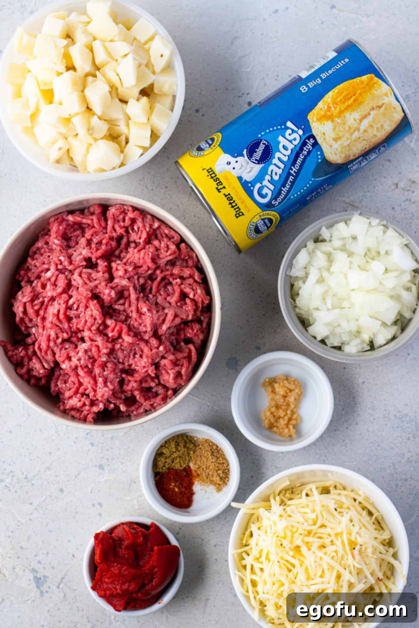 canned biscuits, ground beef, chopped potatoes, diced onion, minced garlic cloves, tomato paste, ground cumin, seasoning salt, smoked paprika, pepper jack cheese ready for assembly.