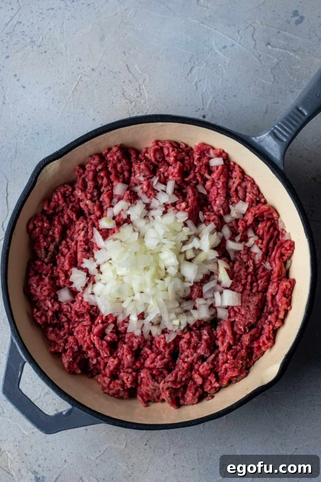 Ground beef and onion cooking in a large skillet, being crumbled.