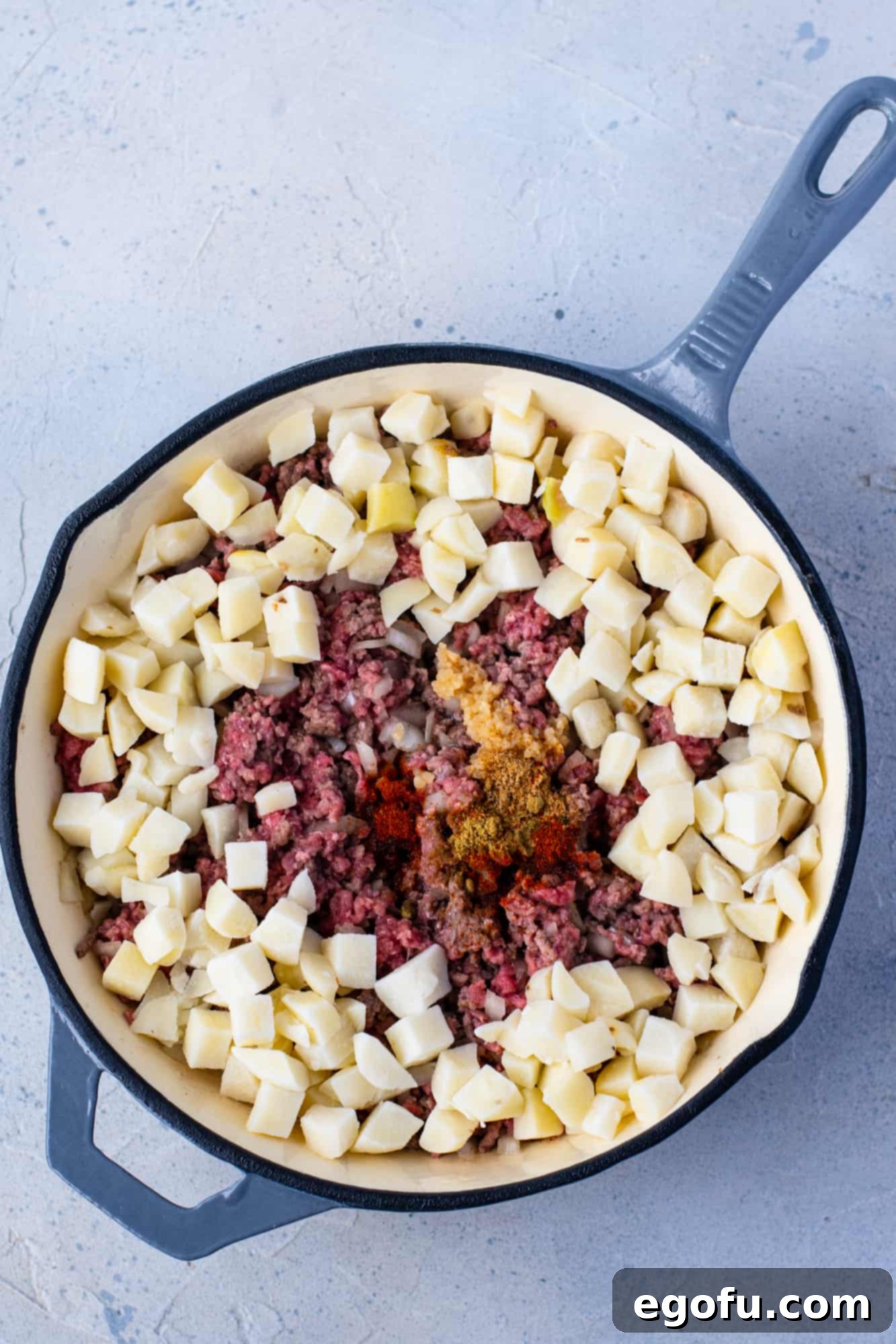 Adding garlic, cumin, seasoning salt, smoked paprika, and diced potatoes to the ground beef mixture in a large skillet.