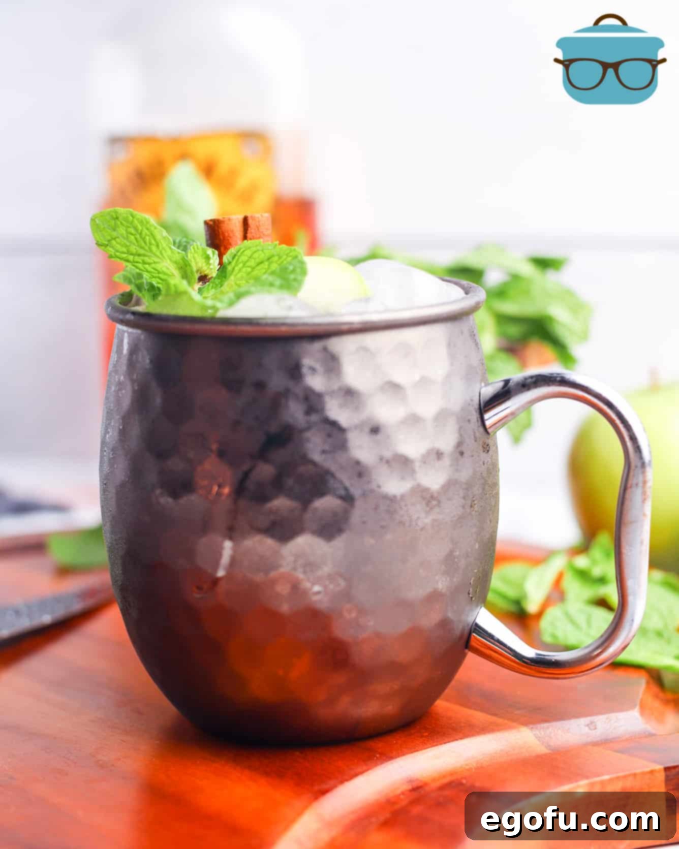 Apple Cider Moscow Mule, shown with a sprig of mint and a bottle of Fireball Cinnamon Whisky in the background.