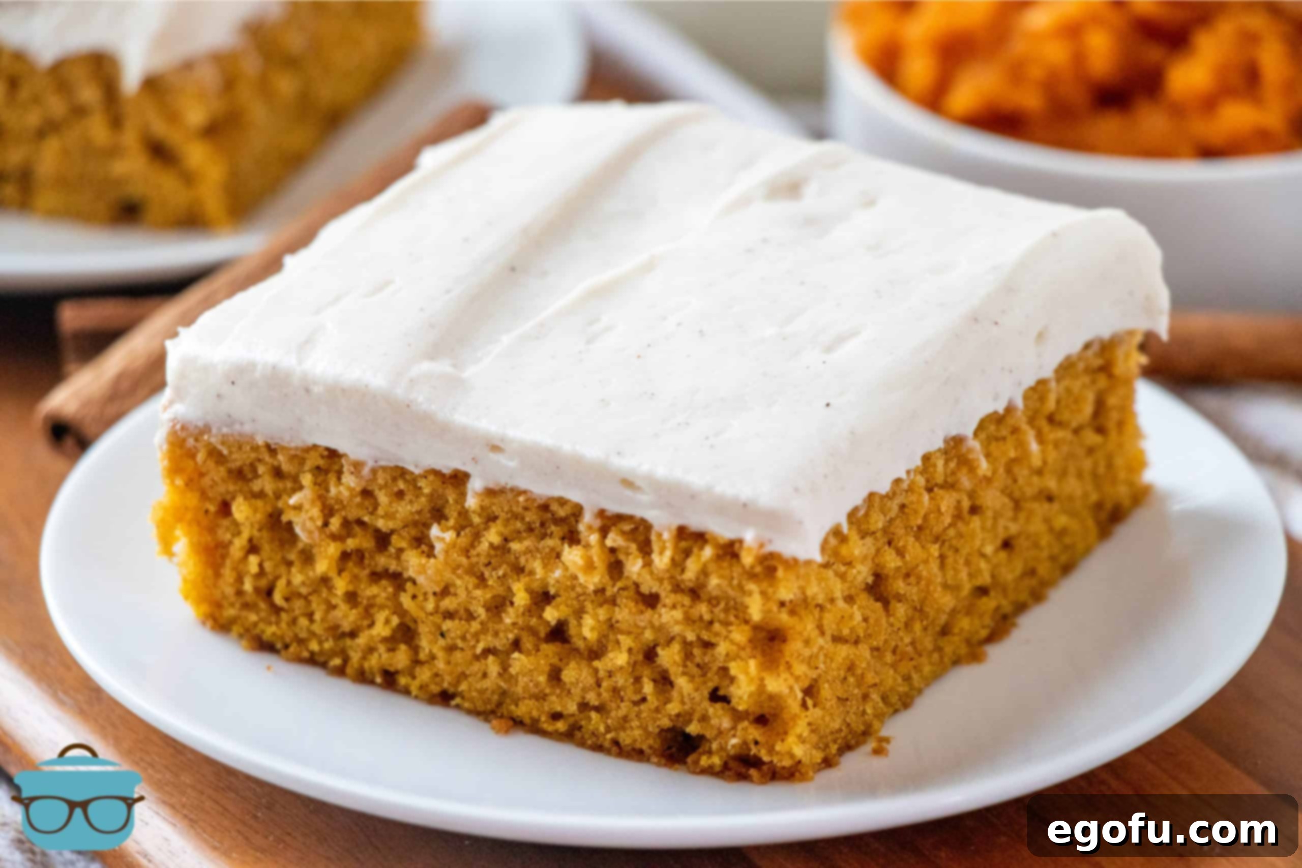 Pumpkin cake bar slice on a small white plate with a bowl of pumpkin puree in a bowl in the background.