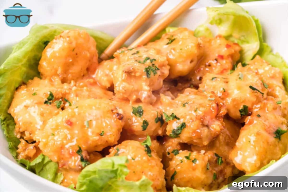 Perfectly cooked Air Fryer Bang Bang Shrimp served on a bed of fresh lettuce in a white bowl with chopsticks, ready to eat.