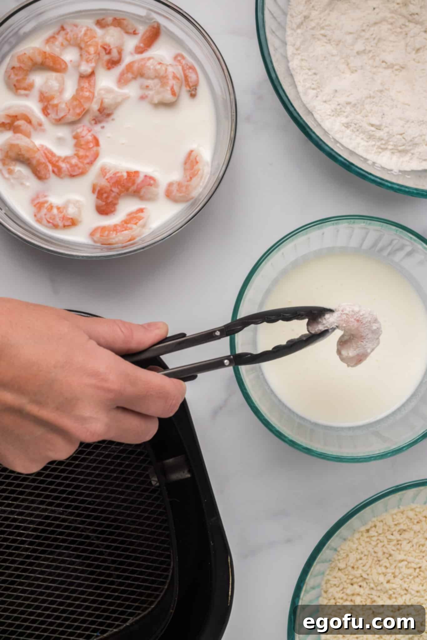 Detailed shot of the breading process, showing buttermilk-soaked shrimp being dipped first in flour, then buttermilk, and finally coated with panko bread crumbs.