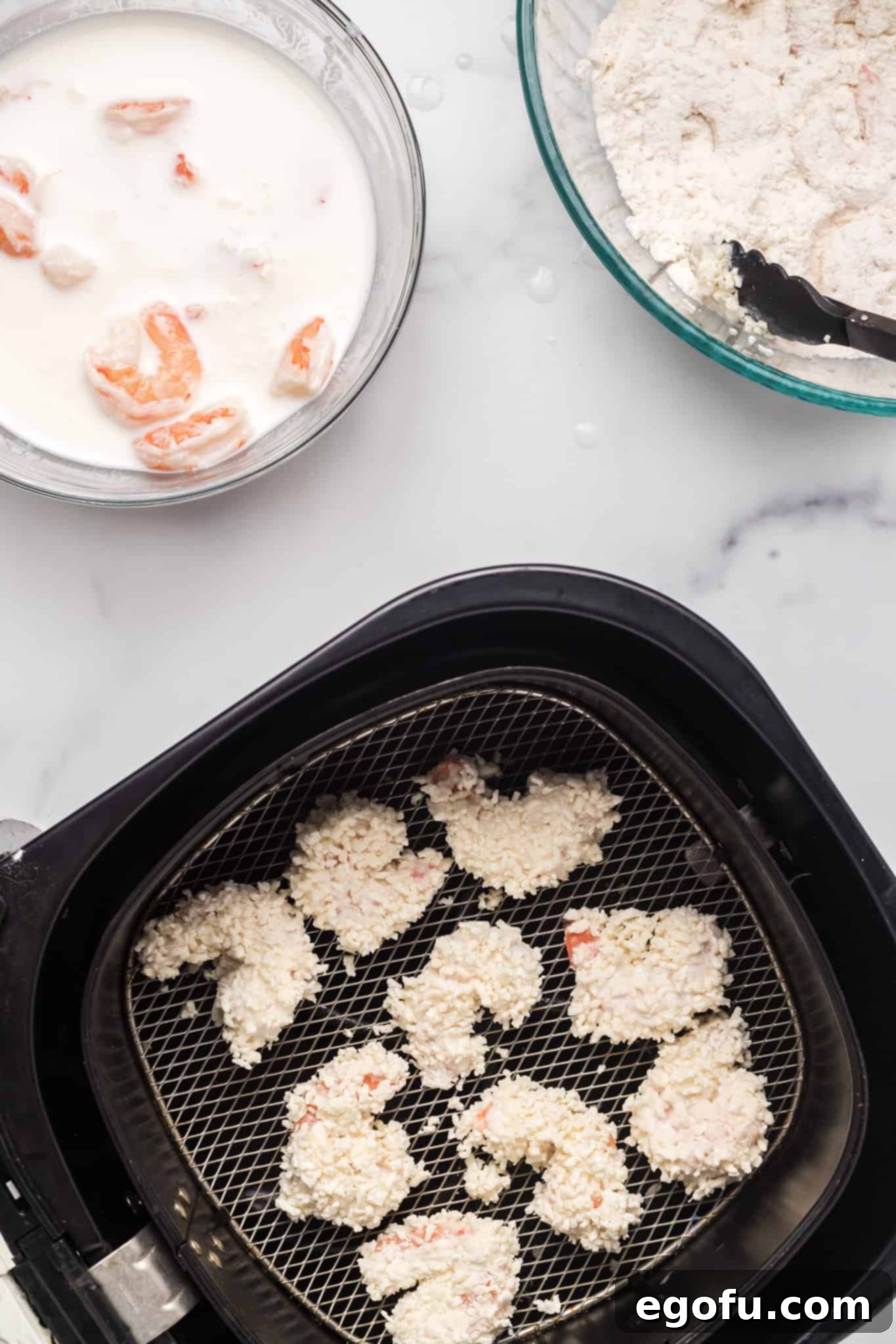 Crispy panko-crusted shrimp carefully arranged in a single layer at the bottom of an air fryer basket, ready for cooking.