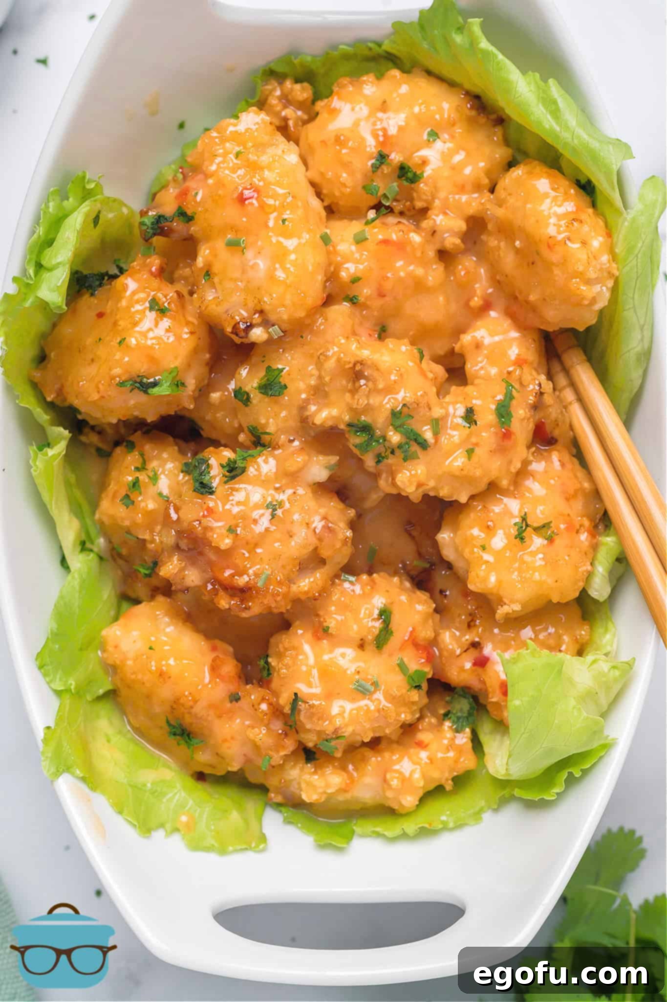Air Fryer Bang Bang Shrimp generously coated in creamy sauce, artfully presented on a large lettuce leaf within a pristine white serving bowl.