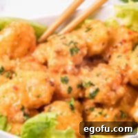 Perfectly cooked Air Fryer Bang Bang Shrimp on a bed of fresh lettuce in a white bowl with chopsticks.