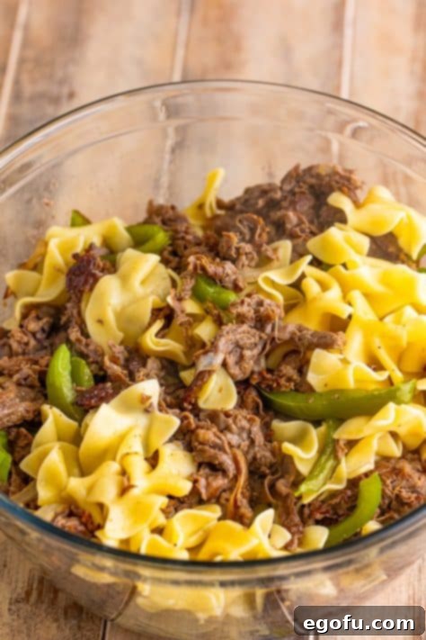 A bowl with pasta, peppers, onions, and ribeye shredded steak mixed together.