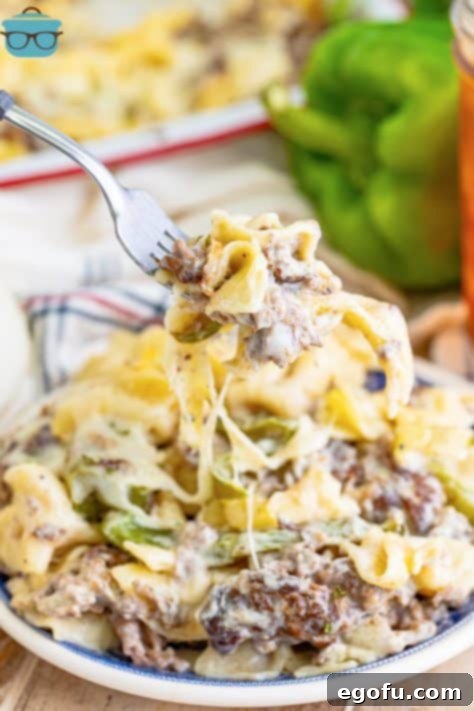 A fork holding a bite of Philly Cheesesteak Casserole over a plate with some more on it.