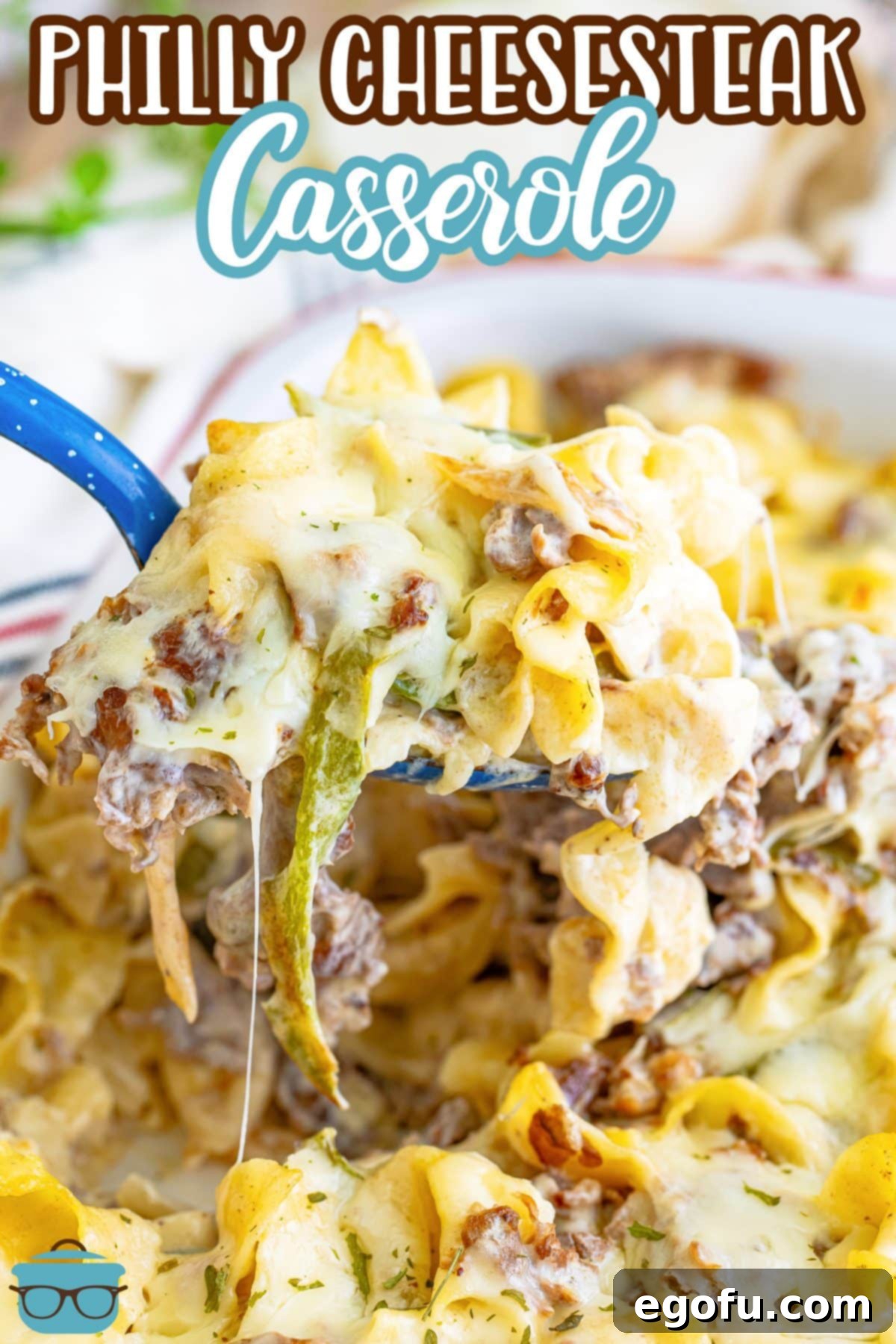 A large helping of Philly Cheesesteak Casserole being held over the casserole dish.