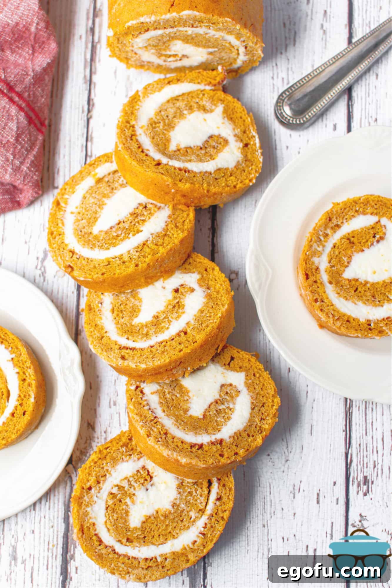 Perfectly sliced homemade pumpkin roll on a rustic wooden cutting board, showcasing its elegant swirl and creamy filling.