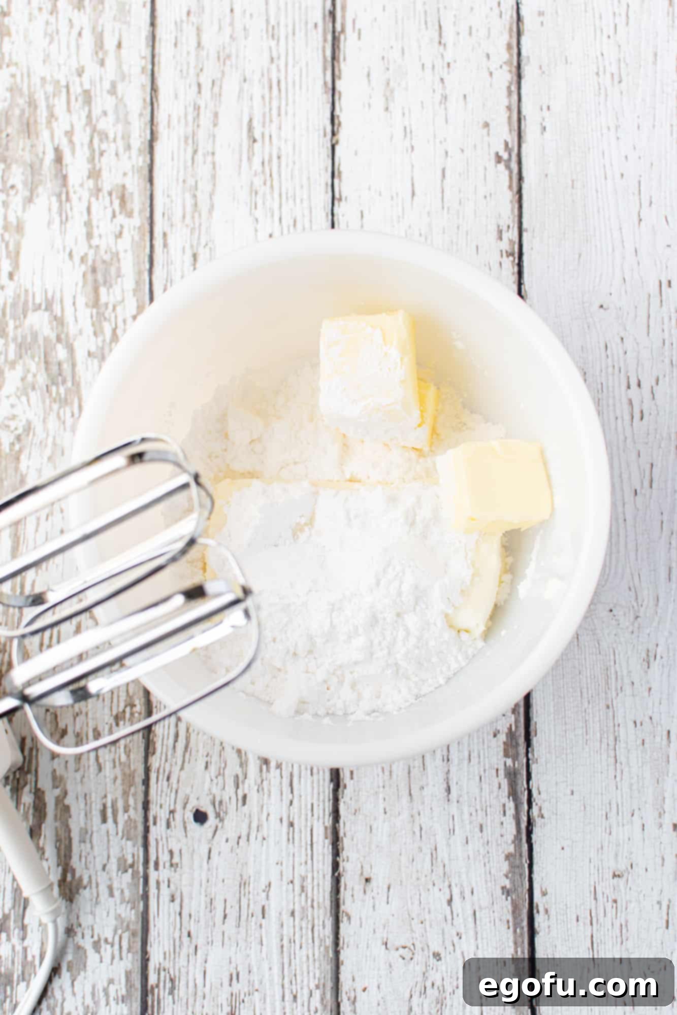Softened cream cheese and butter being beaten with an electric mixer in a white bowl, for the creamy pumpkin roll filling.