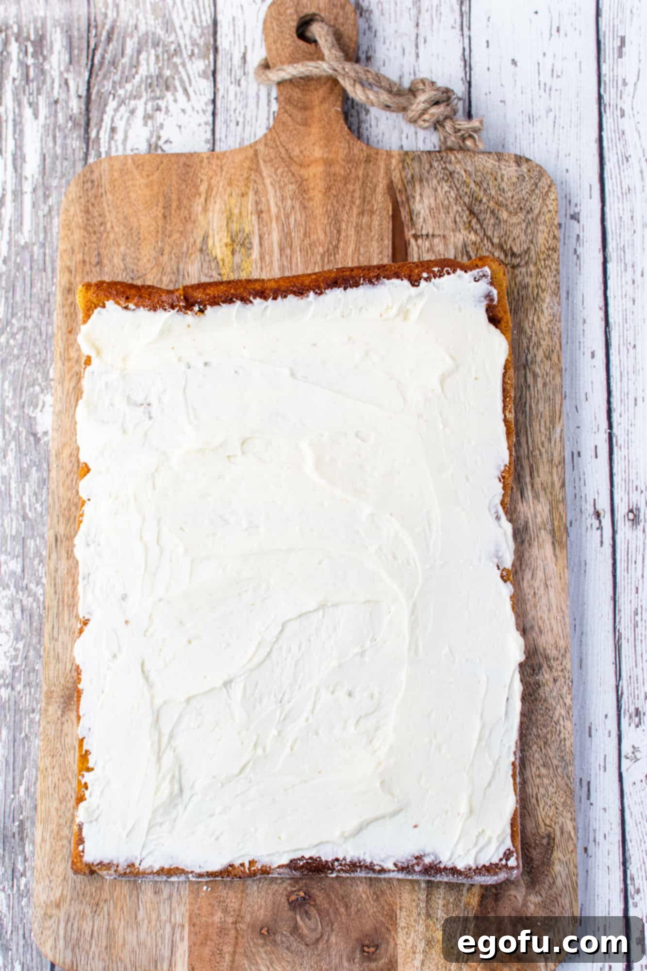 Sweetened cream cheese filling being spread meticulously onto the cooled pumpkin cake, ready for the final roll.