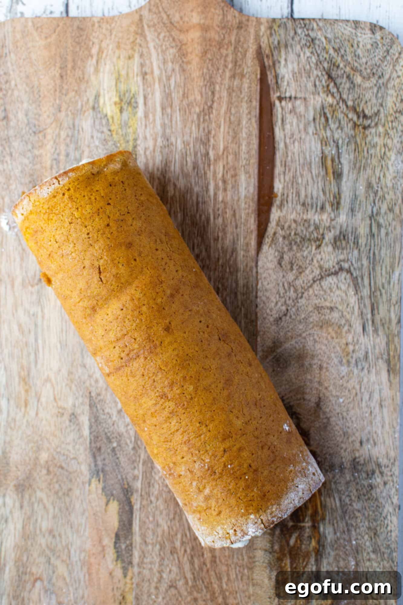 A freshly rolled pumpkin cake with its cream cheese filling, tightly wrapped in plastic wrap and ready for chilling.