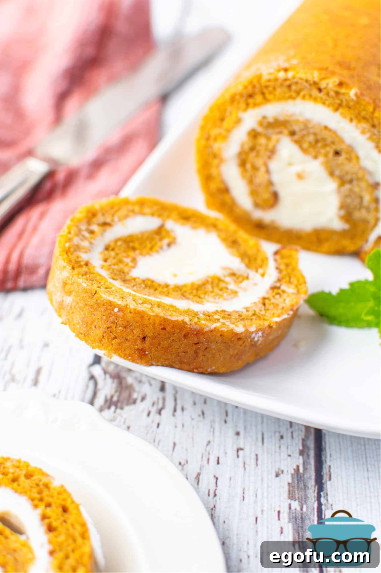 A beautifully presented homemade pumpkin roll on a white platter, with a serving knife nearby, ready for guests.